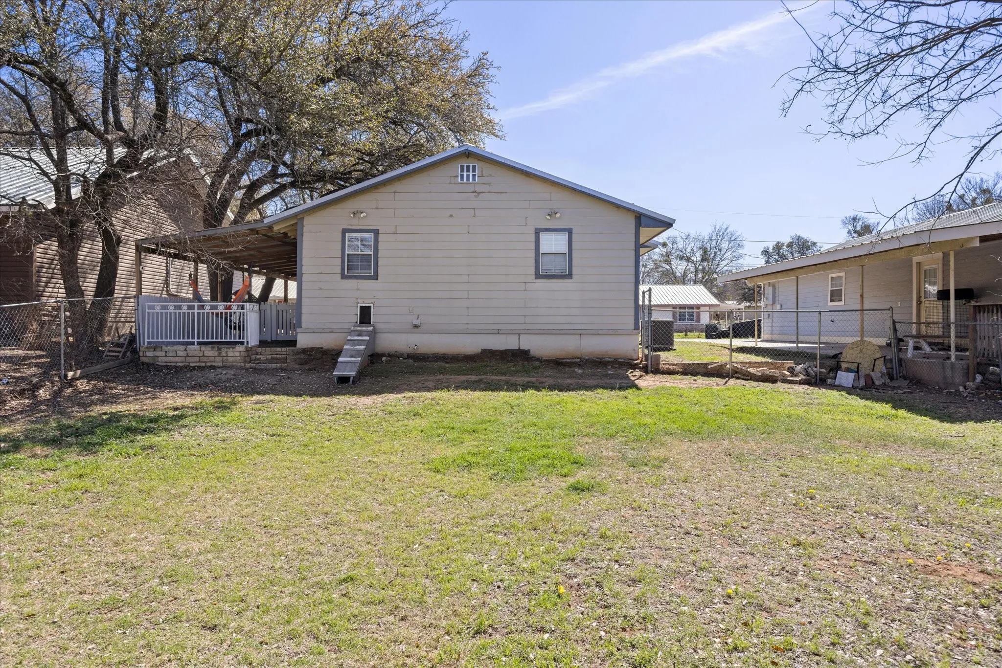 Rear exterior featuring a covered deck with white railing, a chain-link fence, and a spacious grassy yard