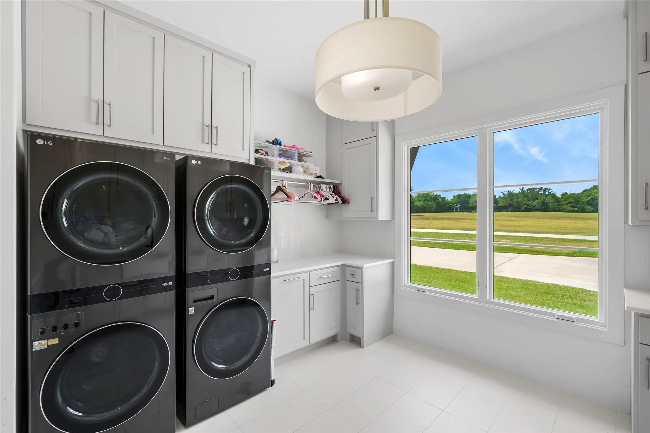 Laundry room featuring white shaker cabinetry, white countertops, tile flooring, a large window, and a drum pendant light fixture