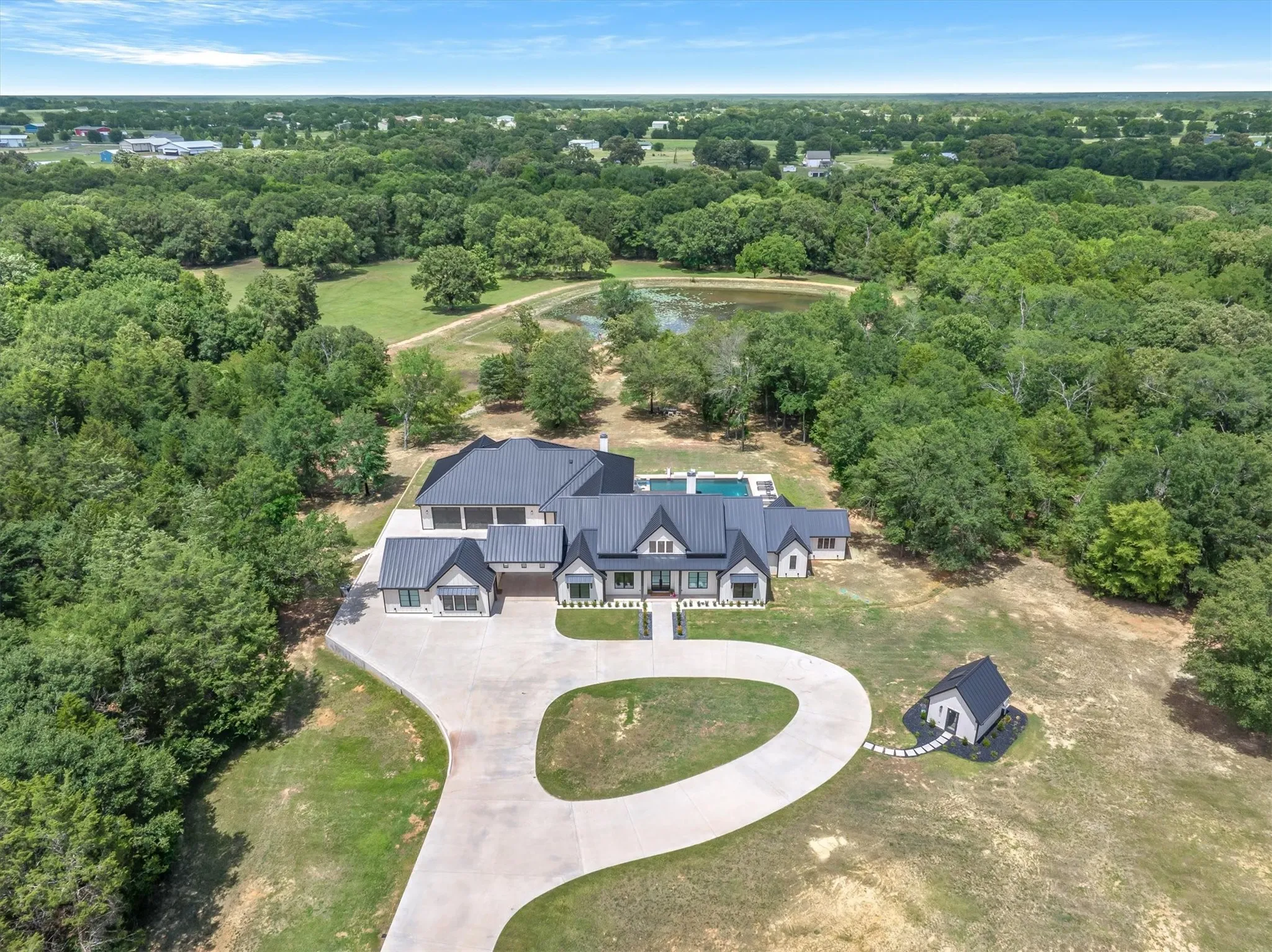 Modern farmhouse architecture with a dark metal roof, a circular drive, and an outdoor swimming pool