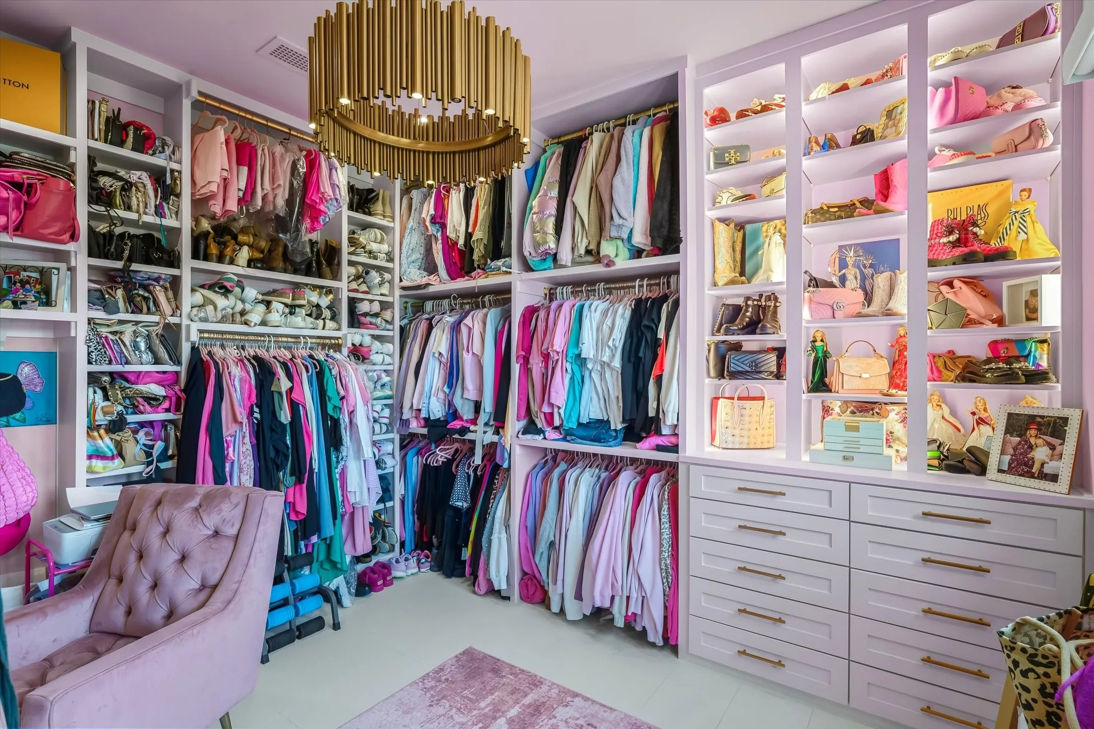 Expansive custom closet featuring extensive built-in shelving, integrated hanging rods, recessed lighting, a central gold-tone chandelier, and light-toned flooring
