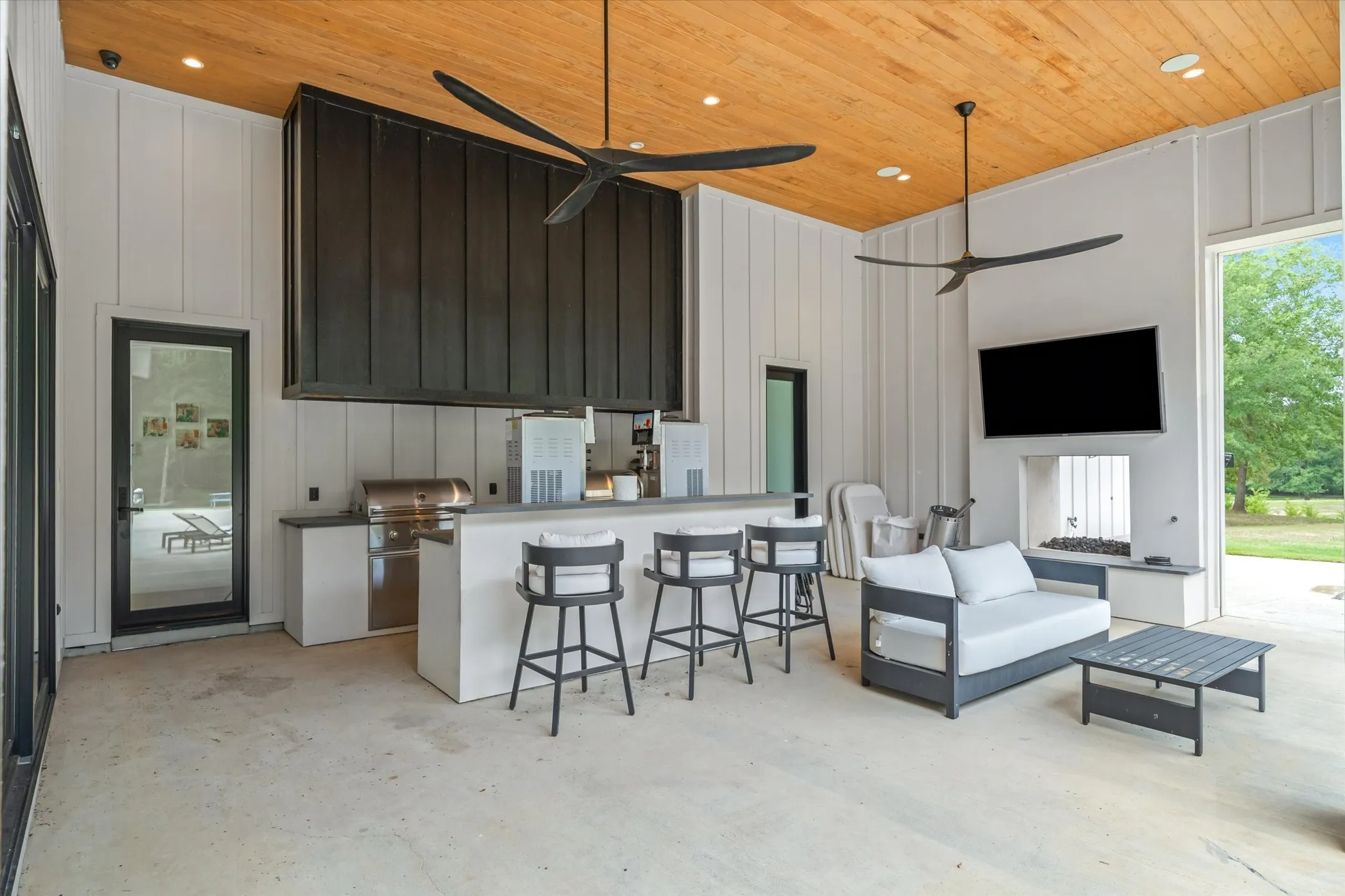 Spacious covered patio featuring a wood-finish plank ceiling, vertical shiplap walls, a built-in outdoor kitchen with a grill, and a fireplace