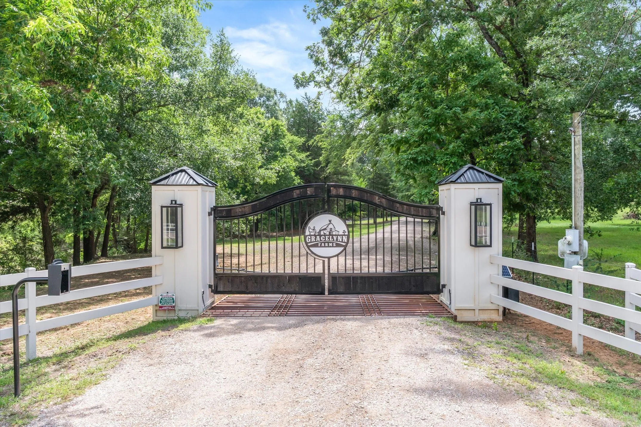 Wrought iron entry gate with decorative medallion, flanked by white pilasters with black lantern fixtures and peaked caps