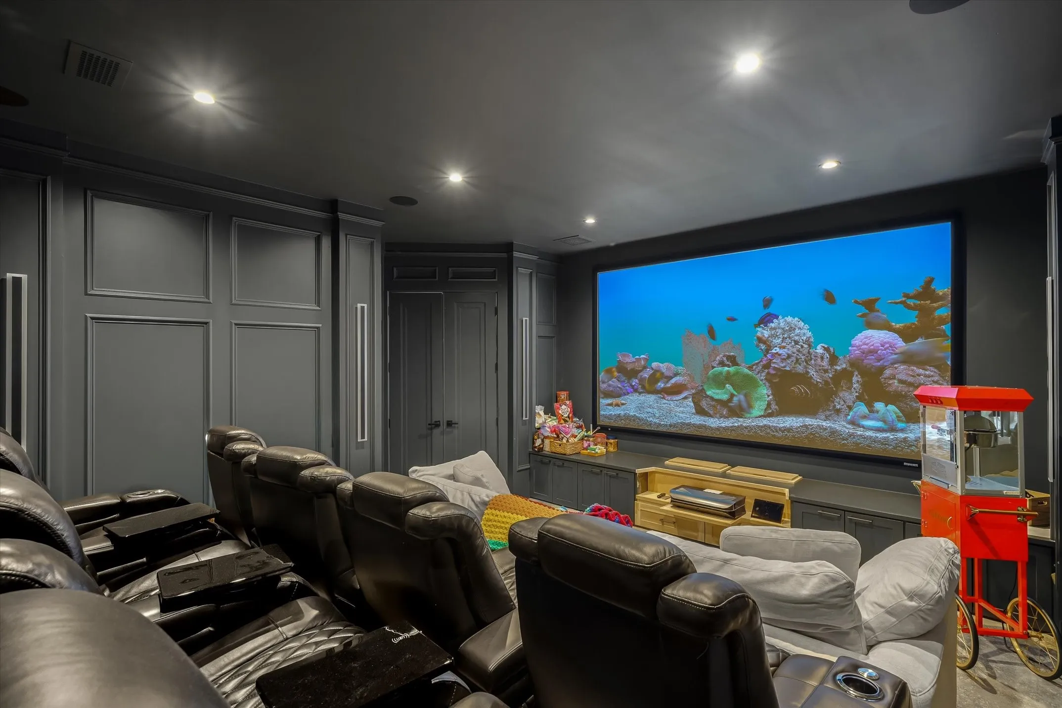 Dedicated media room featuring a large projection screen, dark paneled walls, recessed ceiling lighting, and multiple rows of seating