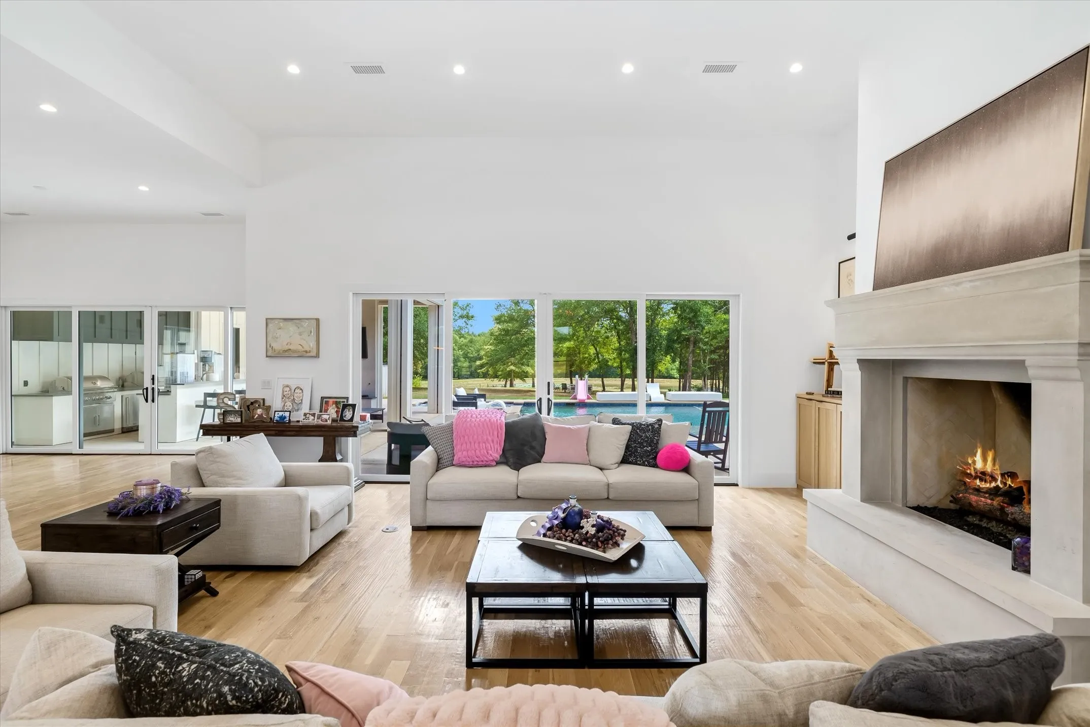 Spacious living area featuring light wood-finish flooring, a large stone fireplace with a hearth, high vaulted ceilings, and recessed lighting