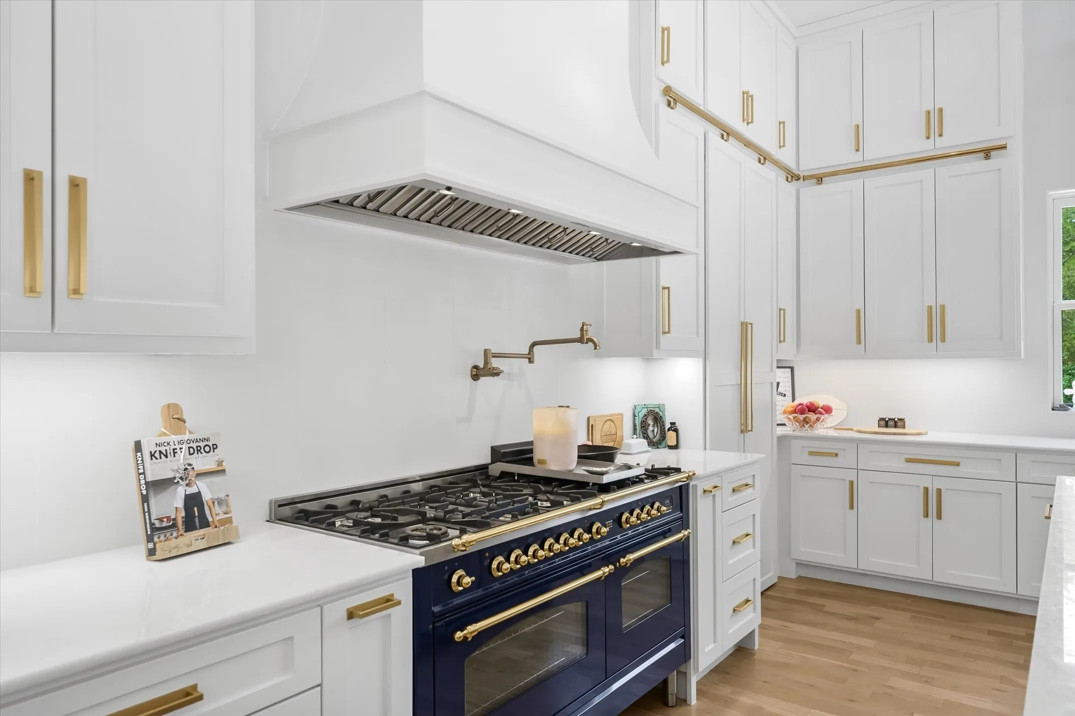 Gourmet kitchen featuring a blue range with brass hardware, white cabinetry, quartz countertops, a matching range hood, and wood-finish flooring