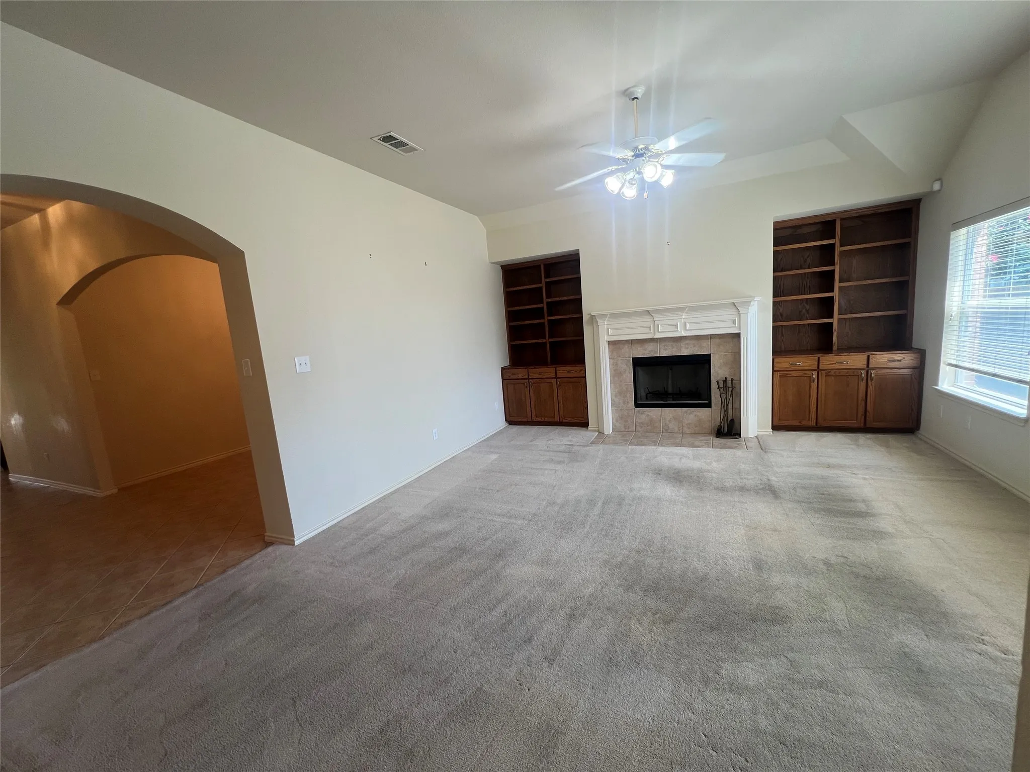 Living area featuring a fireplace with a mantel, built-in shelving, vaulted ceilings, and an arched entry