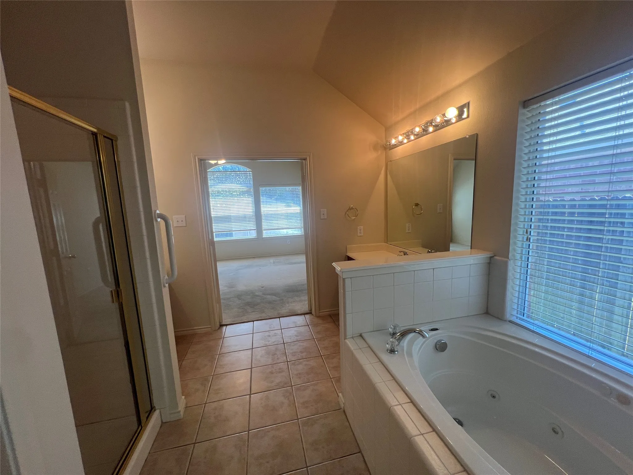 Tiled flooring bathroom featuring a built-in jetted tub, a separate glass-enclosed shower, dual vanity with a large mirror, and a window with horizontal blinds