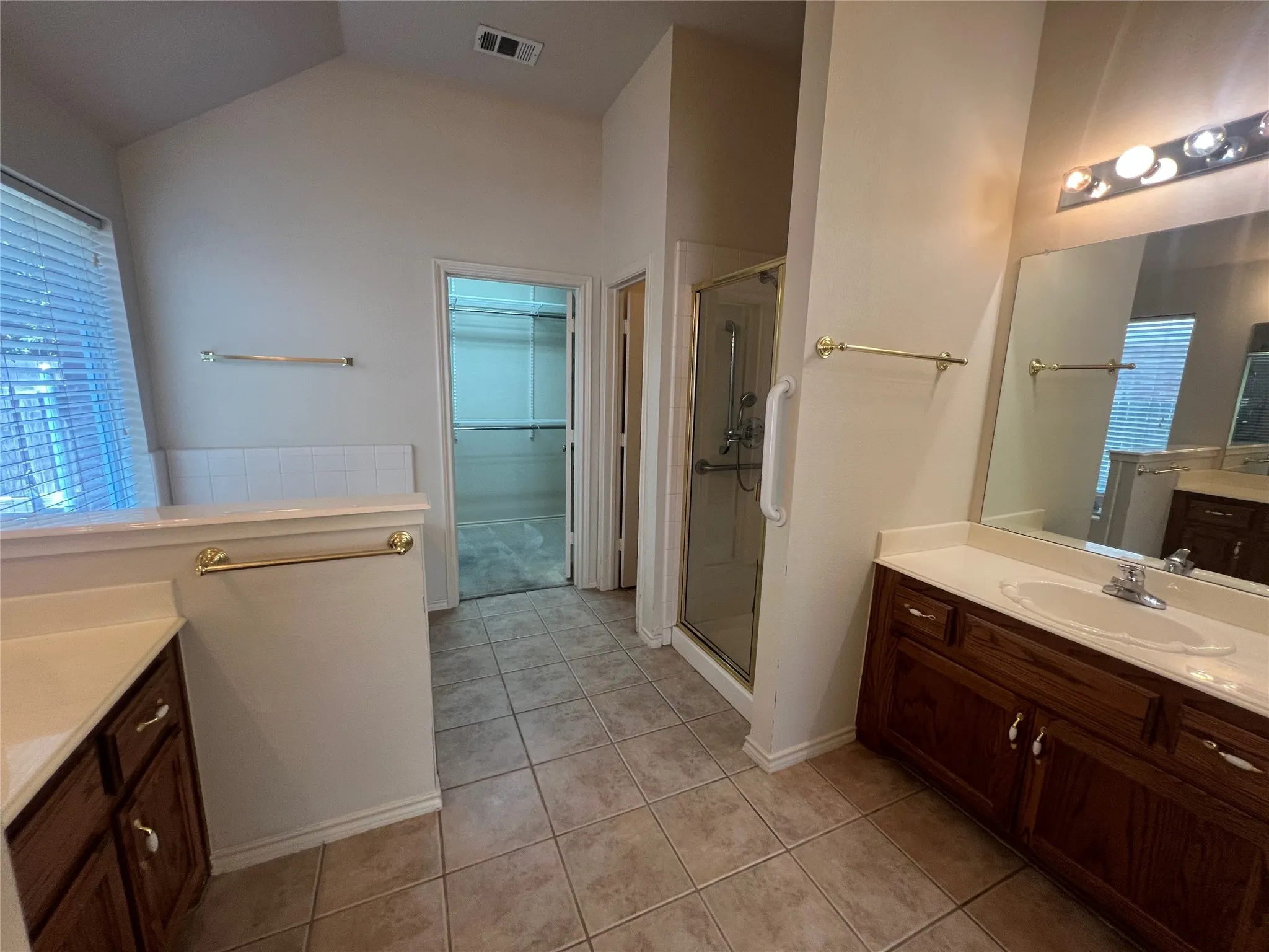 Dual wood-finish vanities with integrated sinks, a glass-enclosed shower, tile flooring, and a walk-in closet
