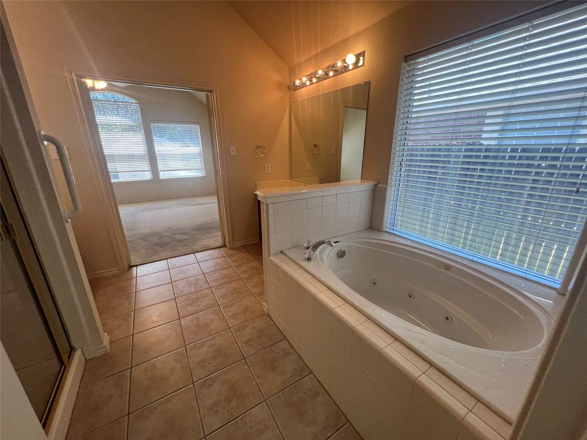 Tiled flooring throughout, featuring a built-in jetted tub, a dual vanity with individual mirrors, and a glass-enclosed shower