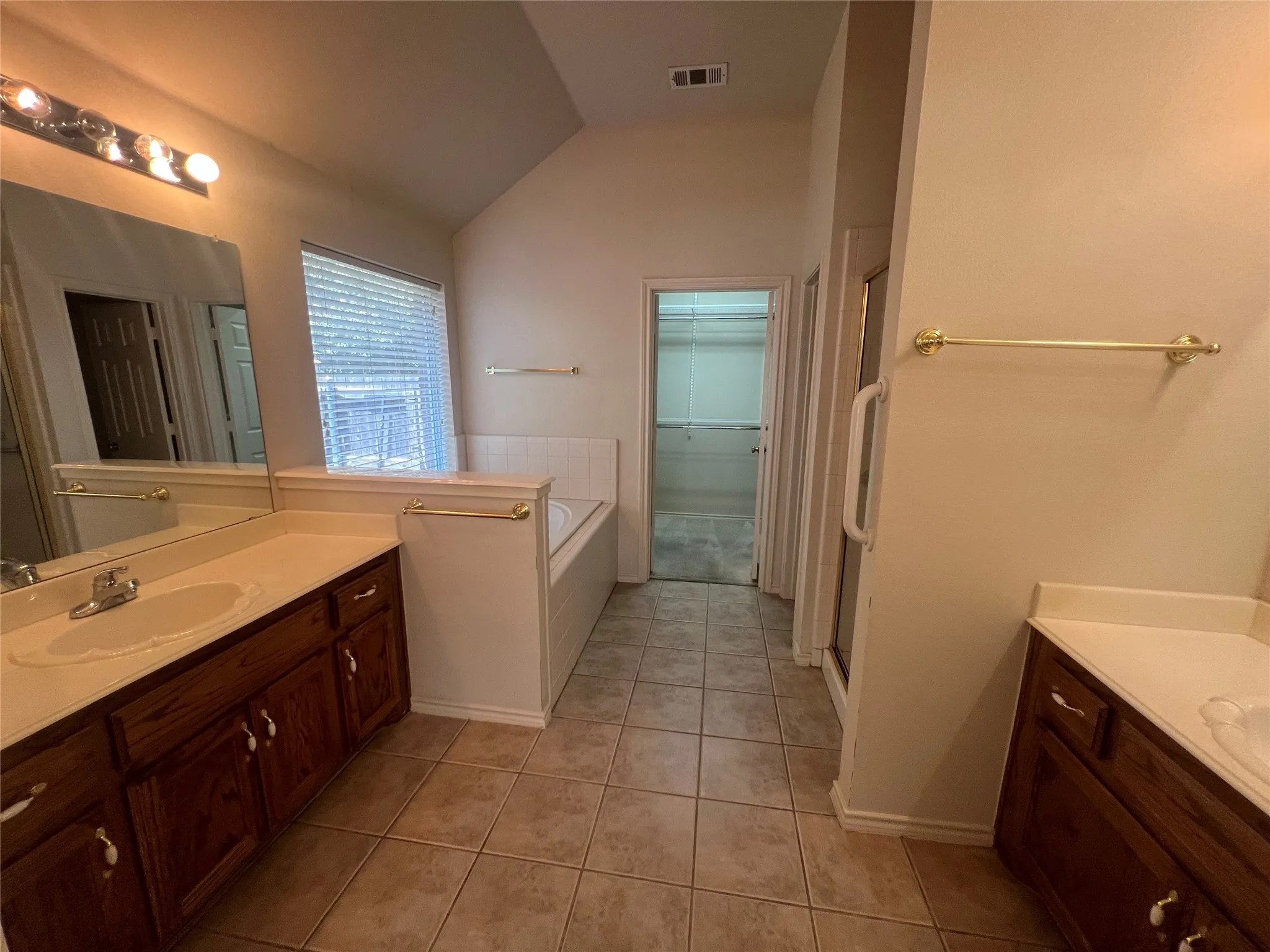 Dual vanity sinks, tile flooring, built-in soaking tub, separate shower enclosure, and an adjacent walk-in closet