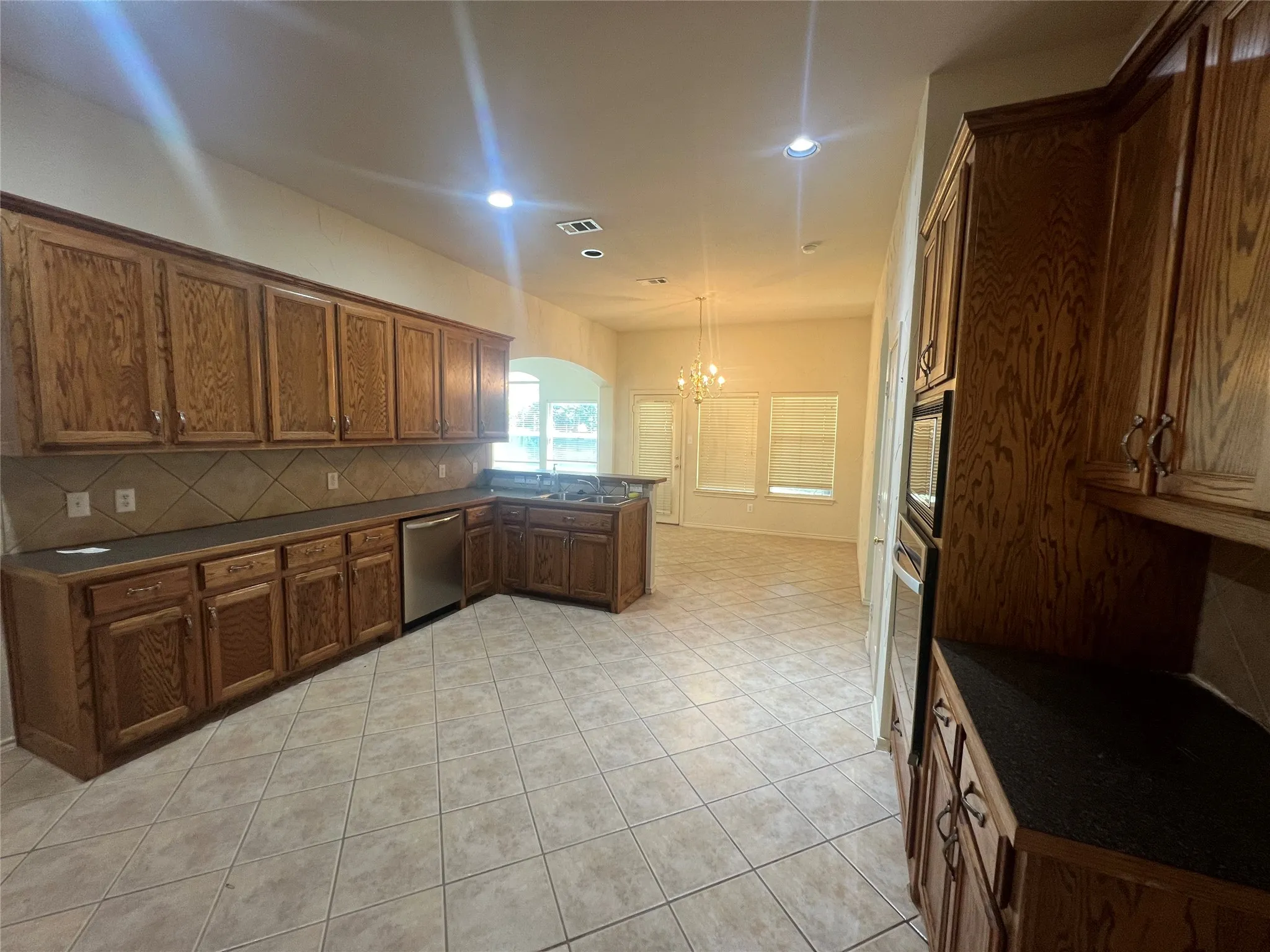 Spacious kitchen featuring extensive wood cabinetry, dark countertops, a tile backsplash, and a stainless steel dishwasher