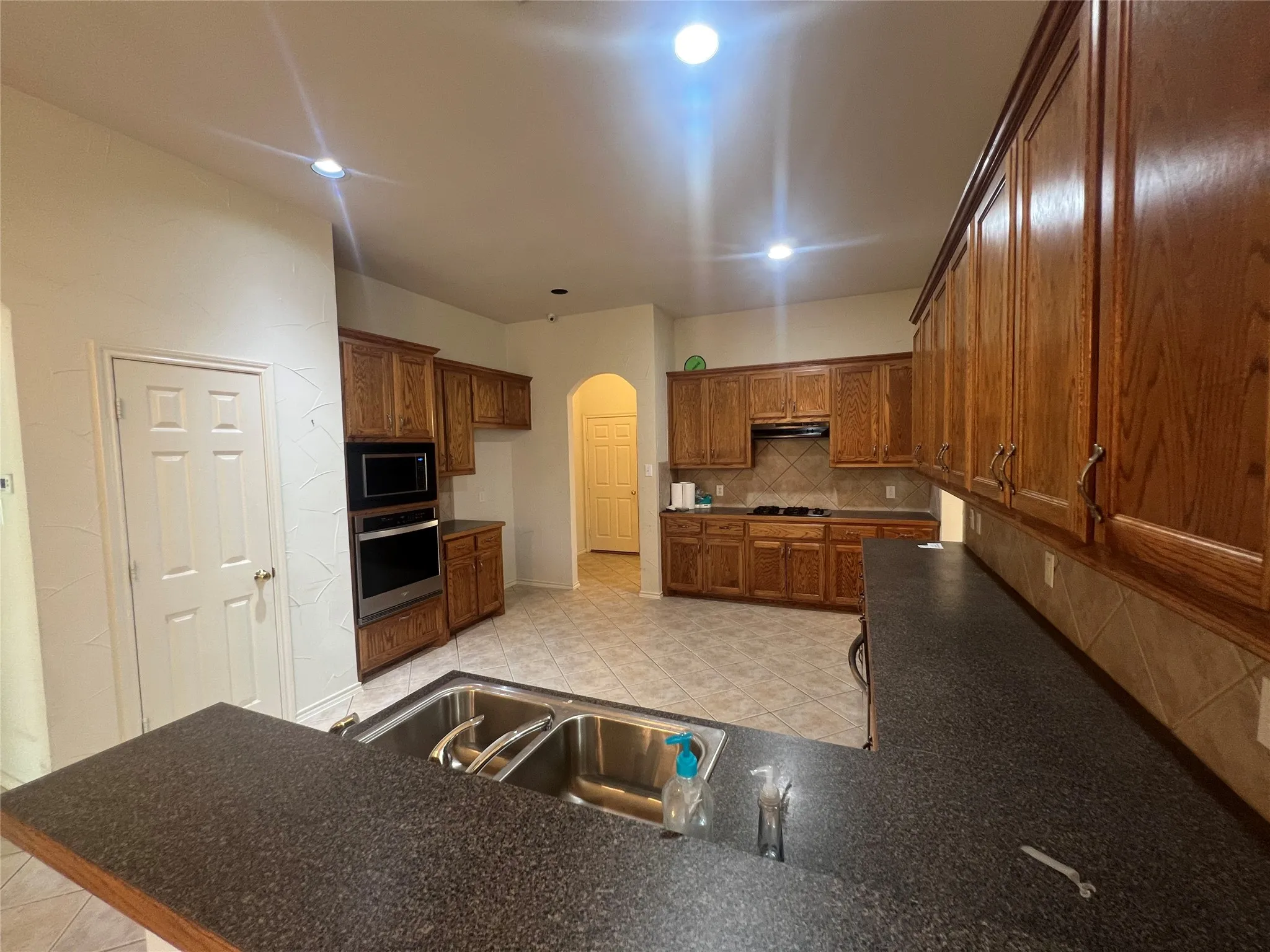 Kitchen featuring wood cabinetry, stainless steel appliances, dark countertops, tile flooring, and recessed lighting