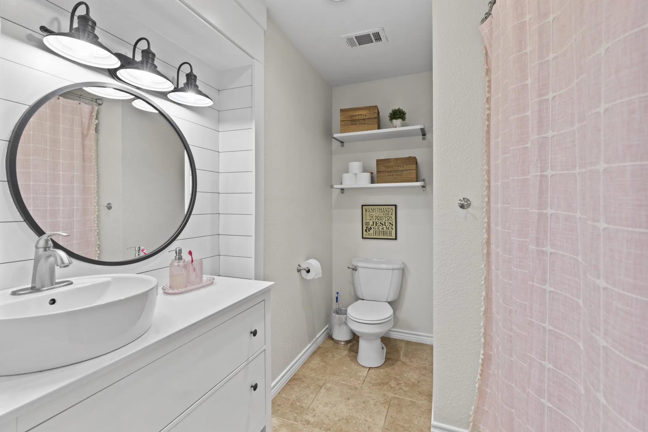 Bathroom featuring shiplap accent wall, vessel sink, round black-framed mirror, and industrial-style vanity lighting