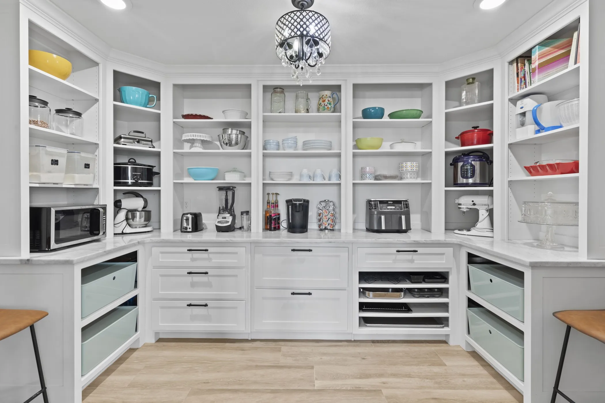Custom built-in white cabinetry with open shelving and closed drawer storage, featuring light-colored stone countertops and light wood-finish flooring