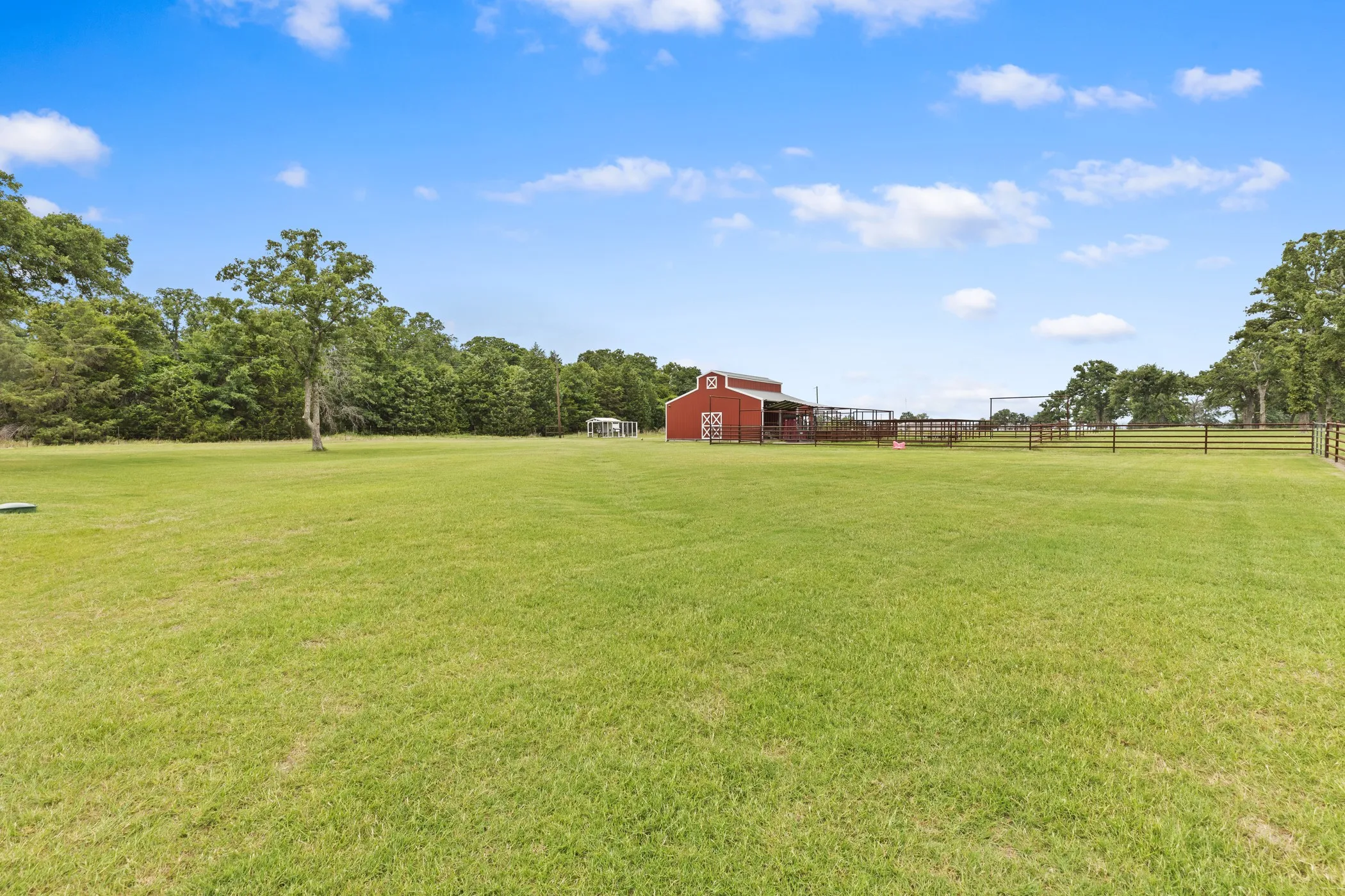 Expansive green lawn with a red barn structure, perimeter fencing, and mature trees
