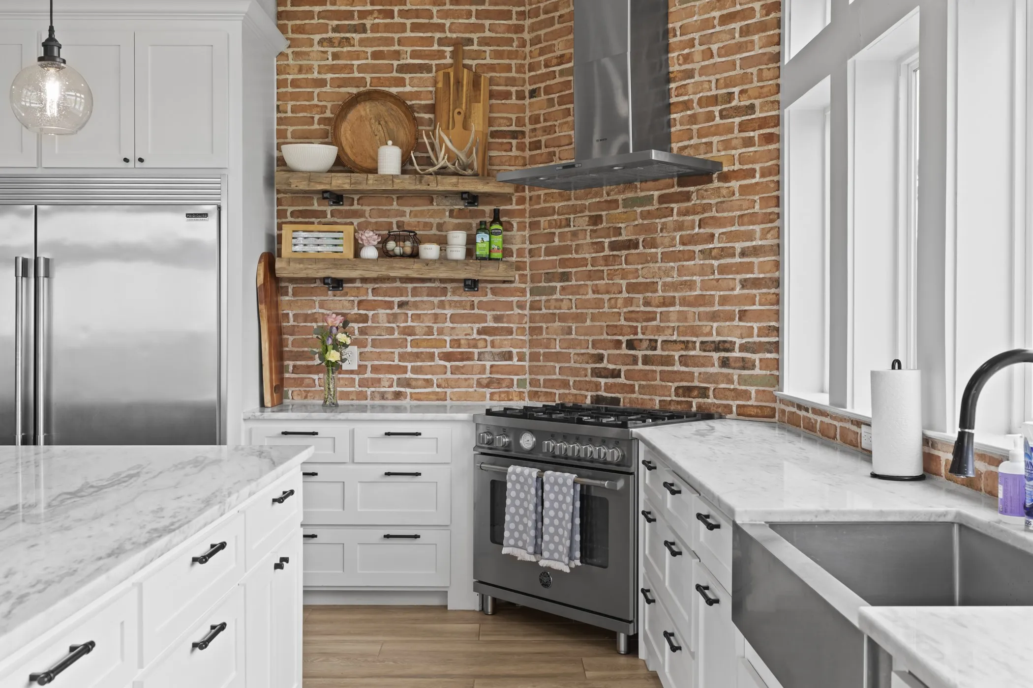 Gourmet kitchen featuring a brick accent wall, professional-grade stainless steel range with hood, integrated full-size refrigerator, and extensive white cabinetry with dark hardware