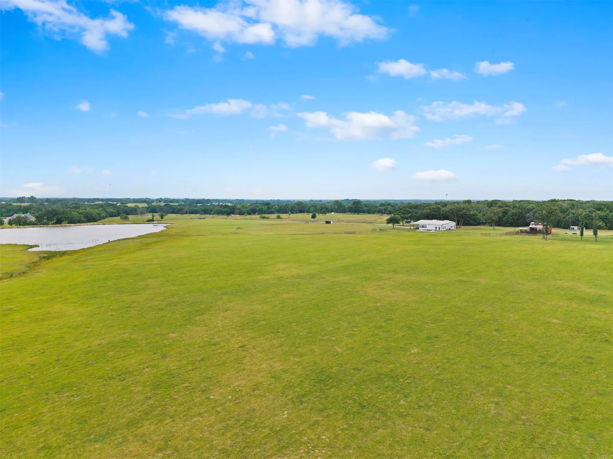 Expansive green acreage featuring a large body of water, distant residential structures, and mature tree lines