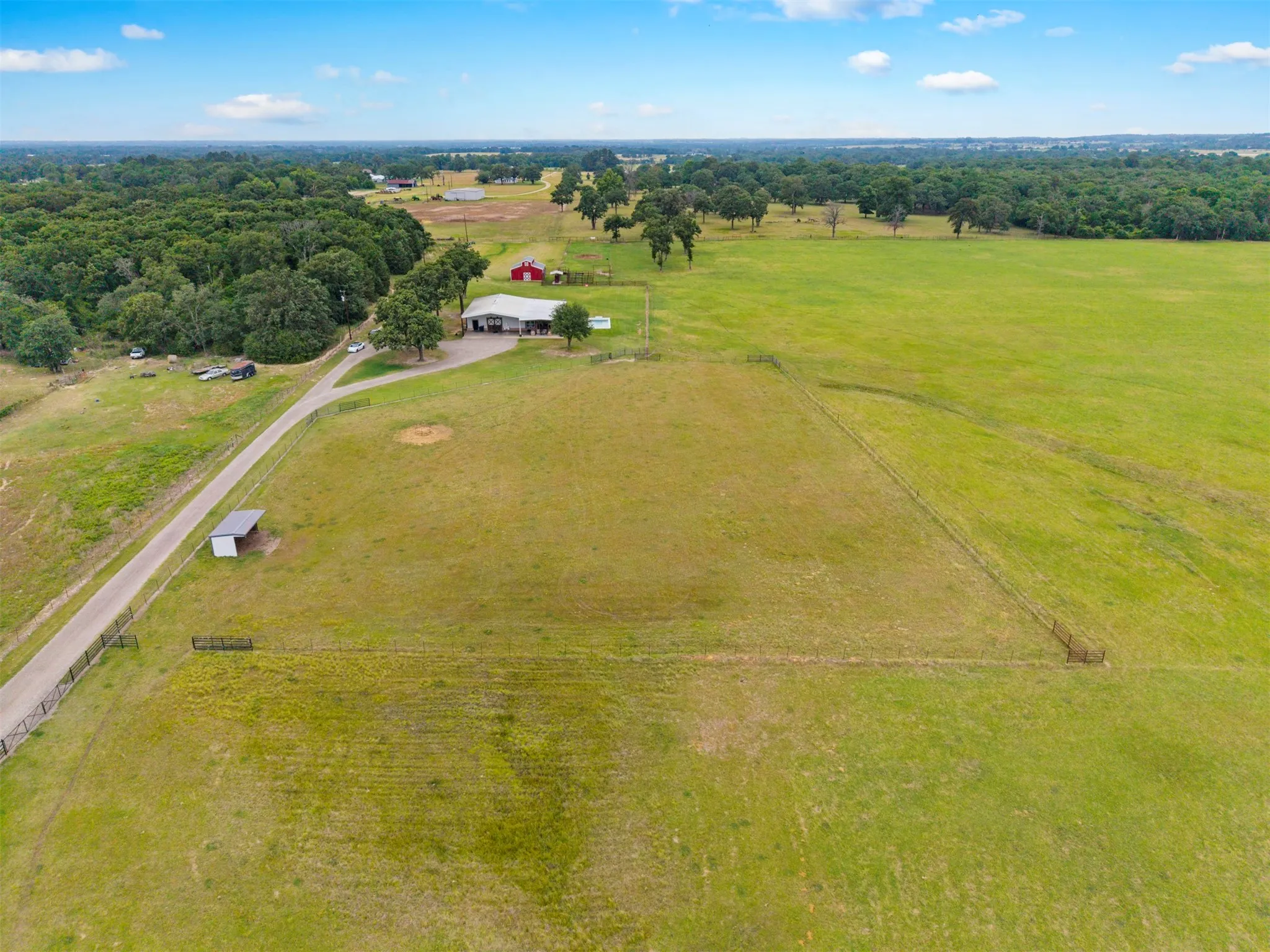 Expansive green fields surrounding a rural property featuring a main residence with a covered porch and a red barn structure