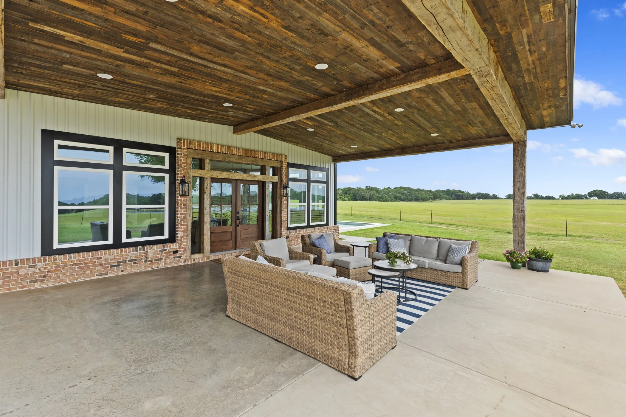 Expansive covered patio featuring a wood-panel ceiling with integrated lighting, exposed wood beams, and a concrete floor