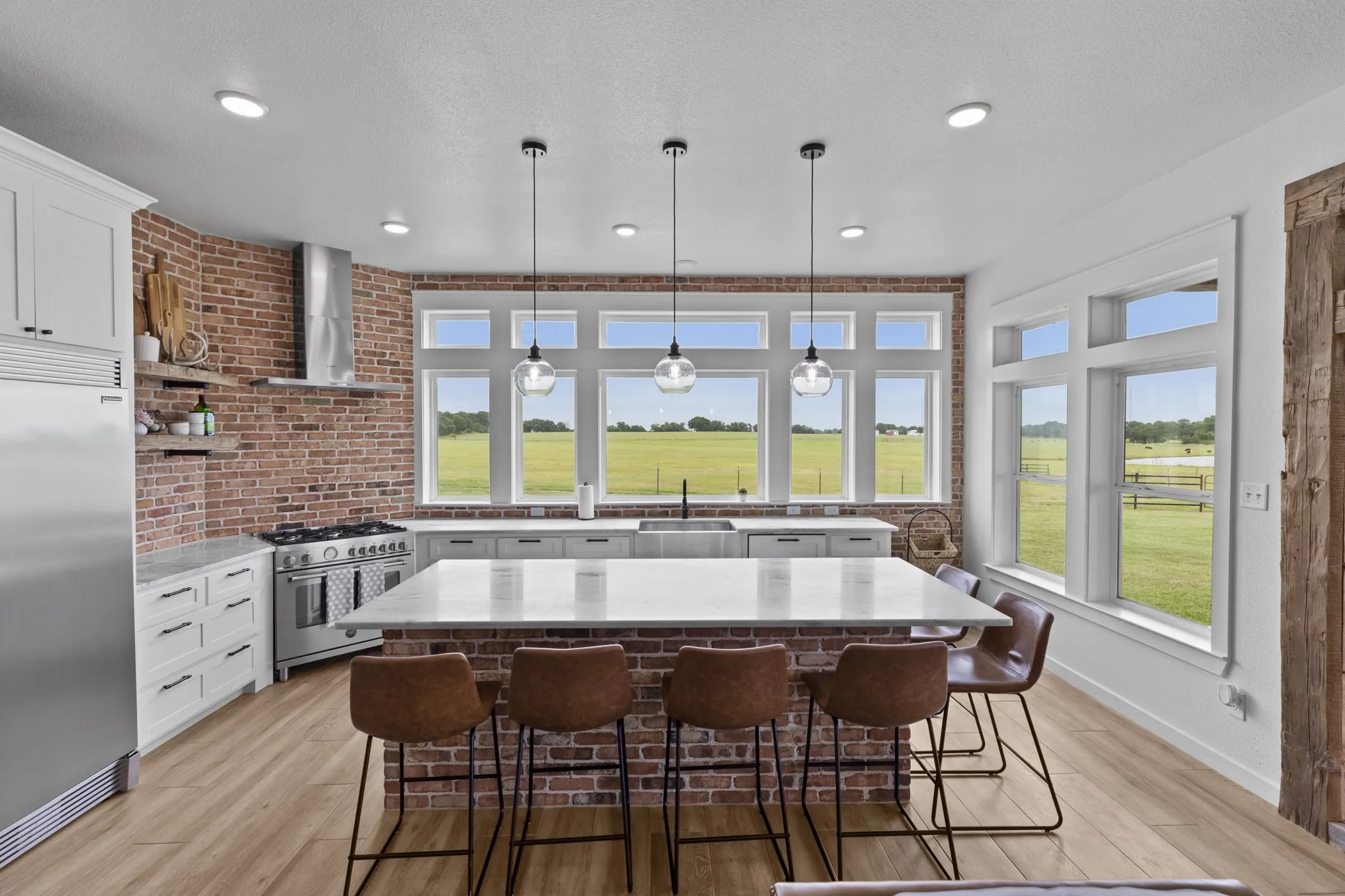 Spacious kitchen featuring an exposed brick accent wall, a large central island with a light-toned countertop, and wood-finish flooring