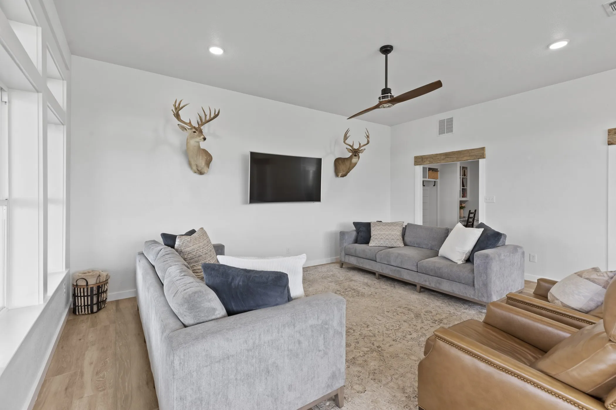 Spacious living area featuring light wood-finish flooring, a contemporary ceiling fan, recessed lighting, and a large window with multiple panes