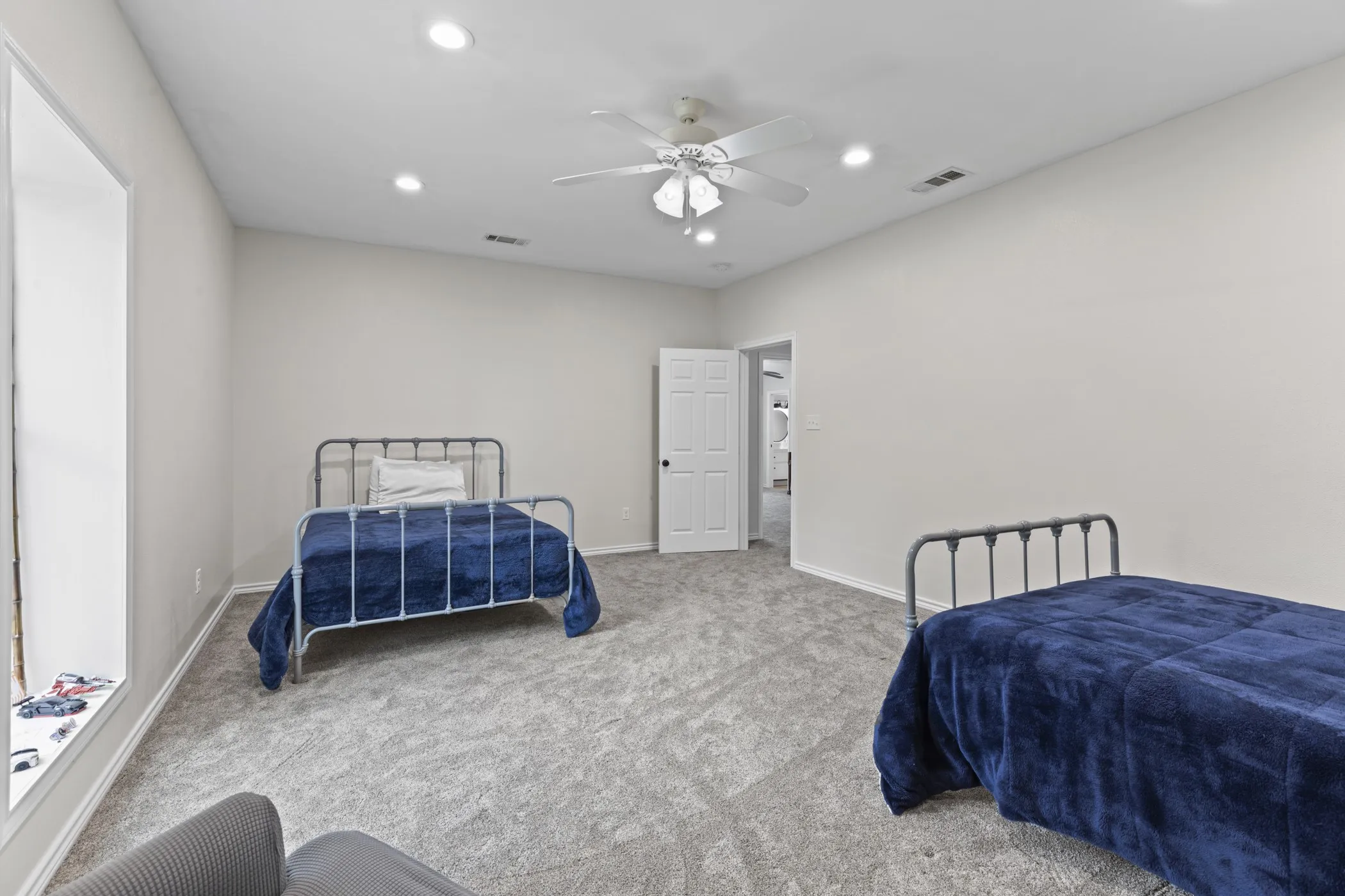 Spacious room featuring light gray walls, gray carpet, and a white ceiling fan with integrated lighting