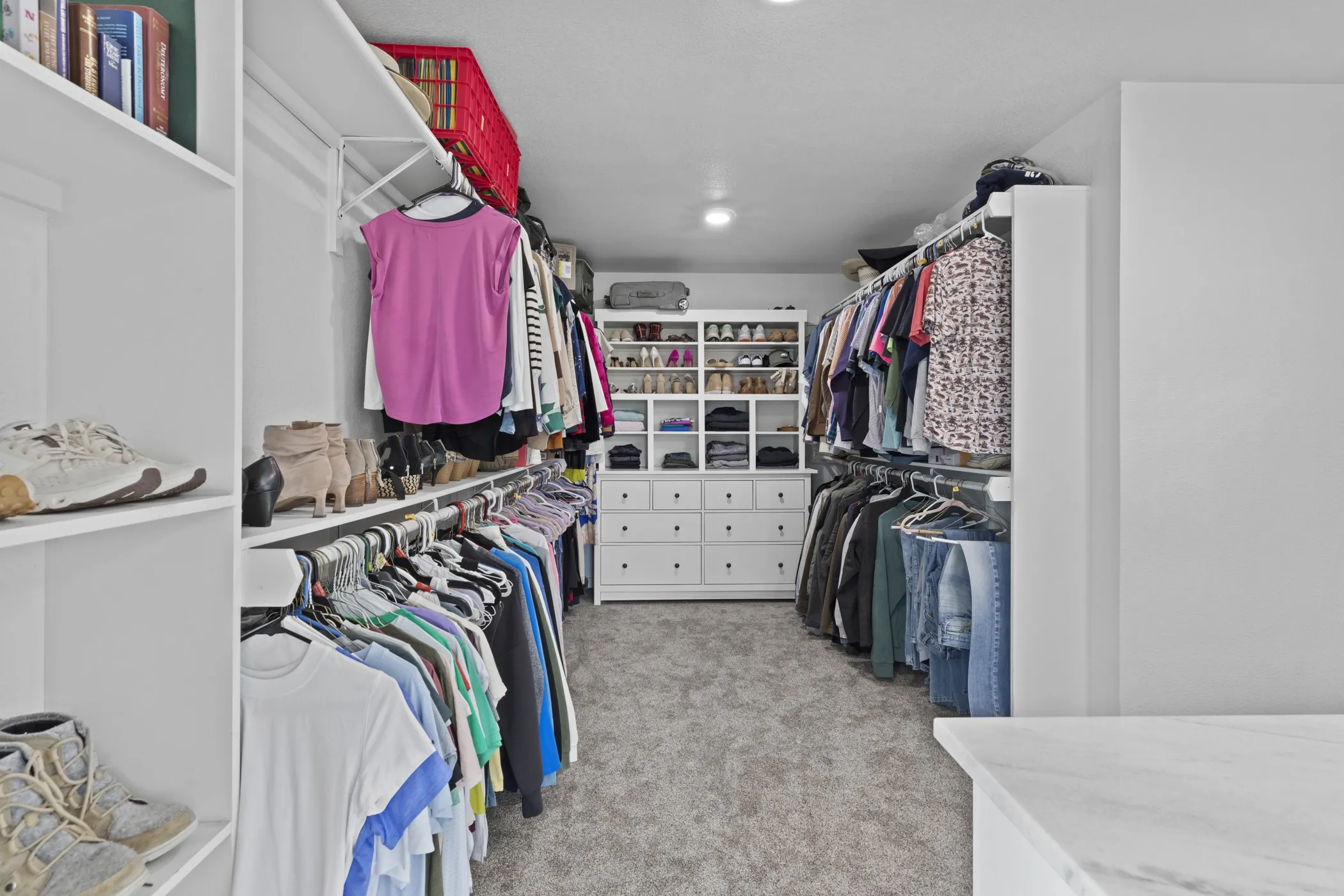 Spacious custom closet featuring extensive built-in shelving, multiple hanging rods, and a central dresser unit with drawers and open compartments