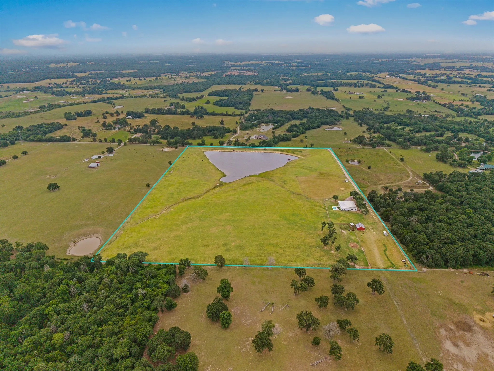 Expansive acreage featuring a substantial pond, a blend of open fields and wooded areas, and a visible structure with a red roof