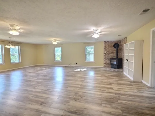 Expansive room featuring wood-finish flooring, a brick accent wall, and a freestanding wood-burning stove