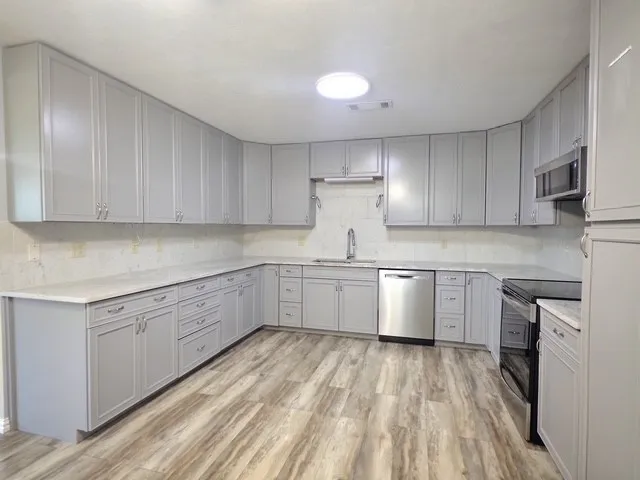 Expansive kitchen featuring light gray shaker cabinetry, light-toned stone countertops, and wood-finish flooring