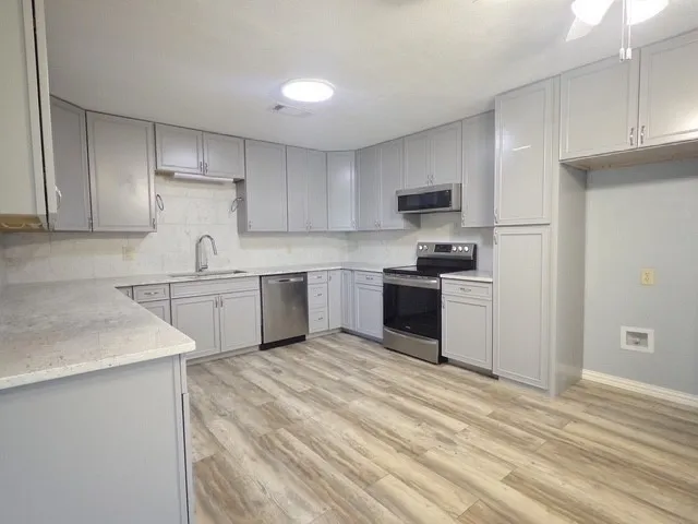 Kitchen featuring light gray cabinetry, stainless steel appliances, wood-finish flooring, light-toned countertops, and a circular ceiling light fixture