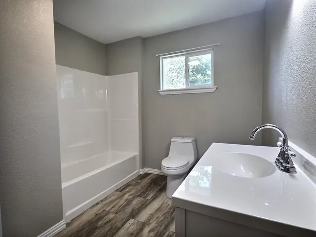 Bathroom featuring a white vanity with integrated sink, chrome faucet, and wood-finish flooring