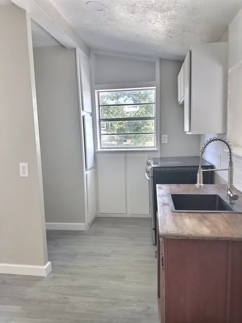 Compact kitchen featuring an integrated sink, wood-finish countertops, and white upper cabinetry