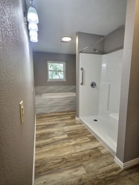 Spacious bathroom featuring a built-in soaking tub with textured tile surround, a separate shower with integrated seating, and wood-finish flooring
