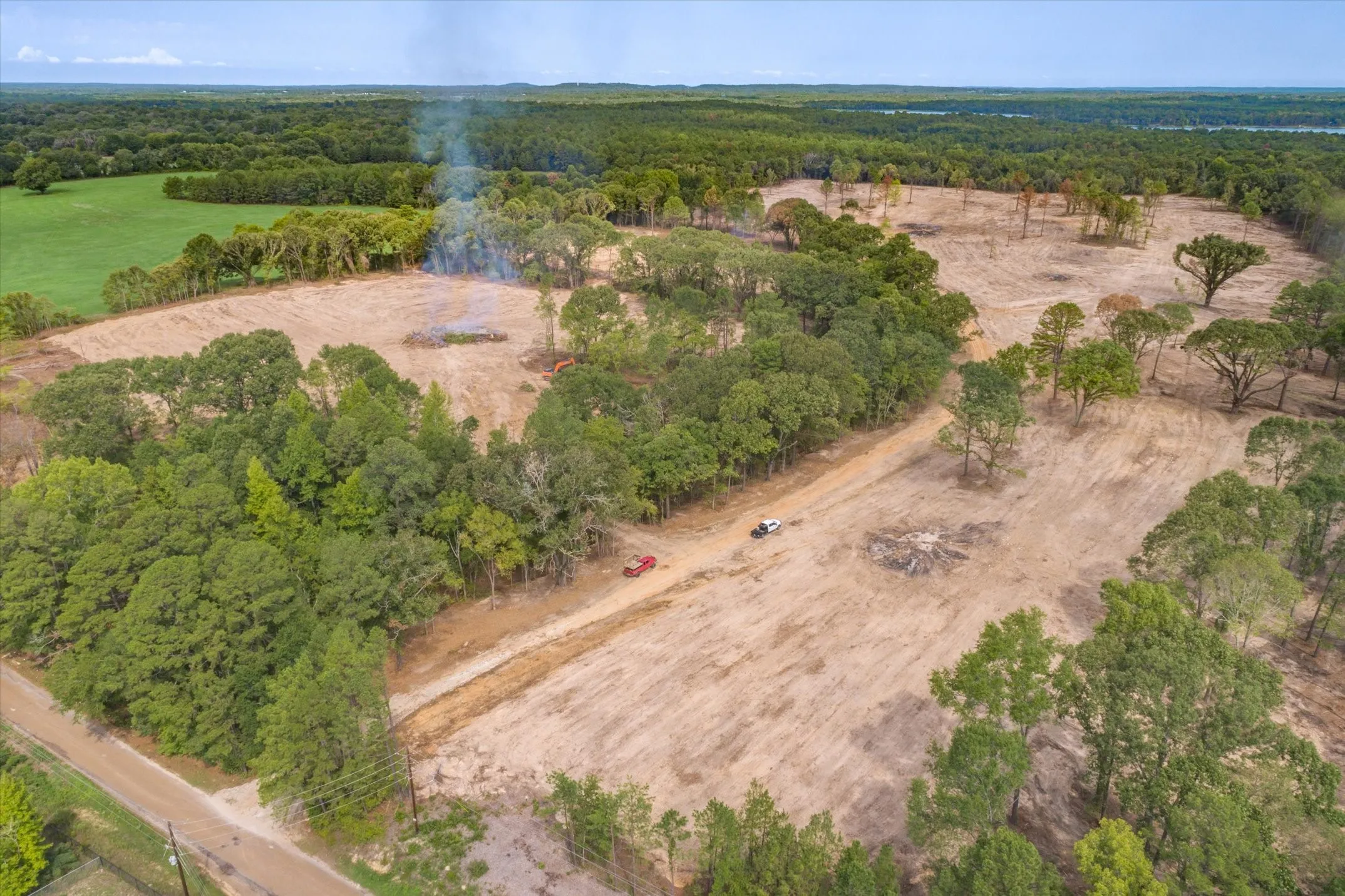Expansive cleared land featuring scattered mature trees, a dirt road, and surrounding dense woodland