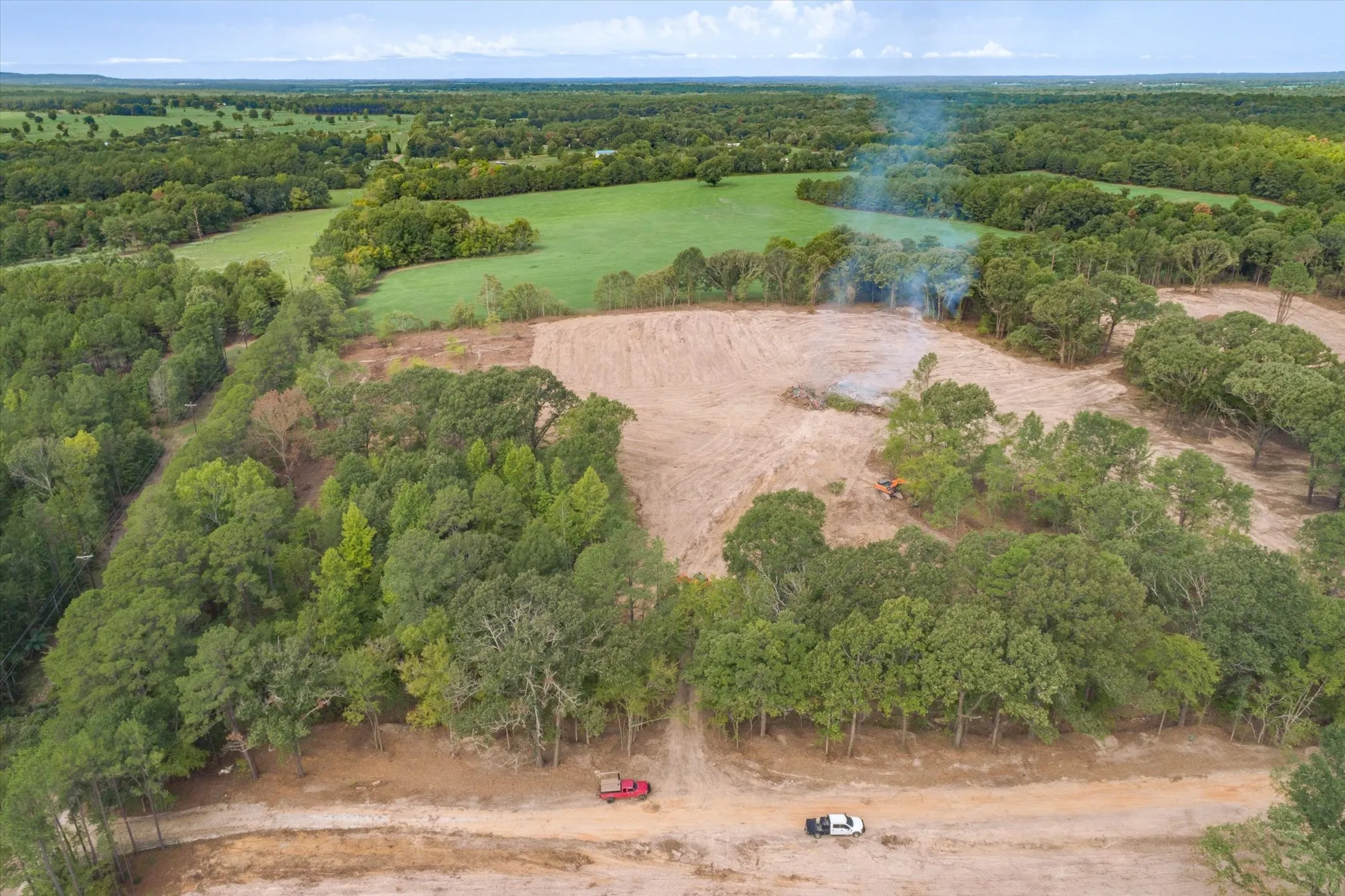 Expansive cleared land featuring surrounding mature trees and varied vegetation