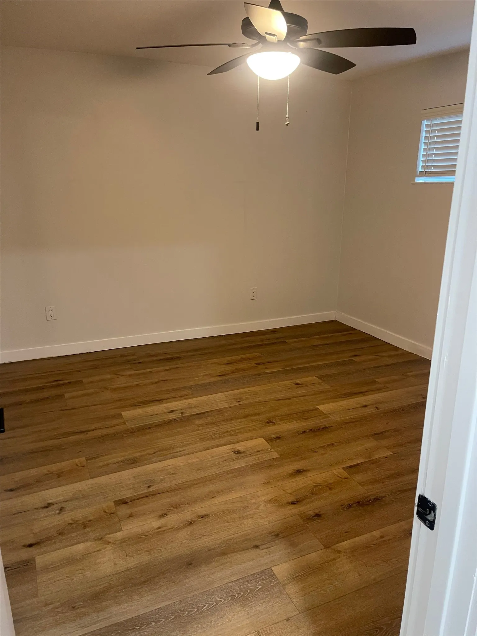 Room featuring wood-finish flooring, a ceiling fan with integrated lighting, and a window with horizontal blinds