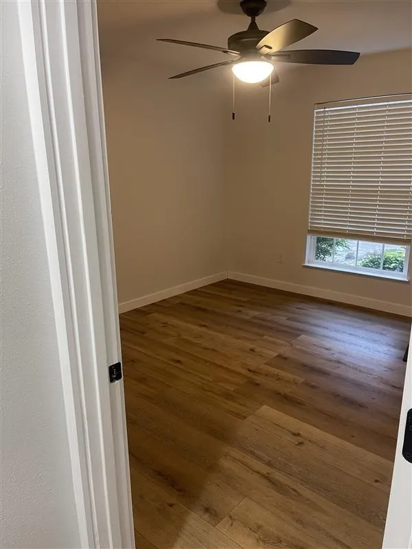 Room featuring wood-finish flooring, a ceiling fan with integrated lighting, window with horizontal blinds, and neutral wall tones