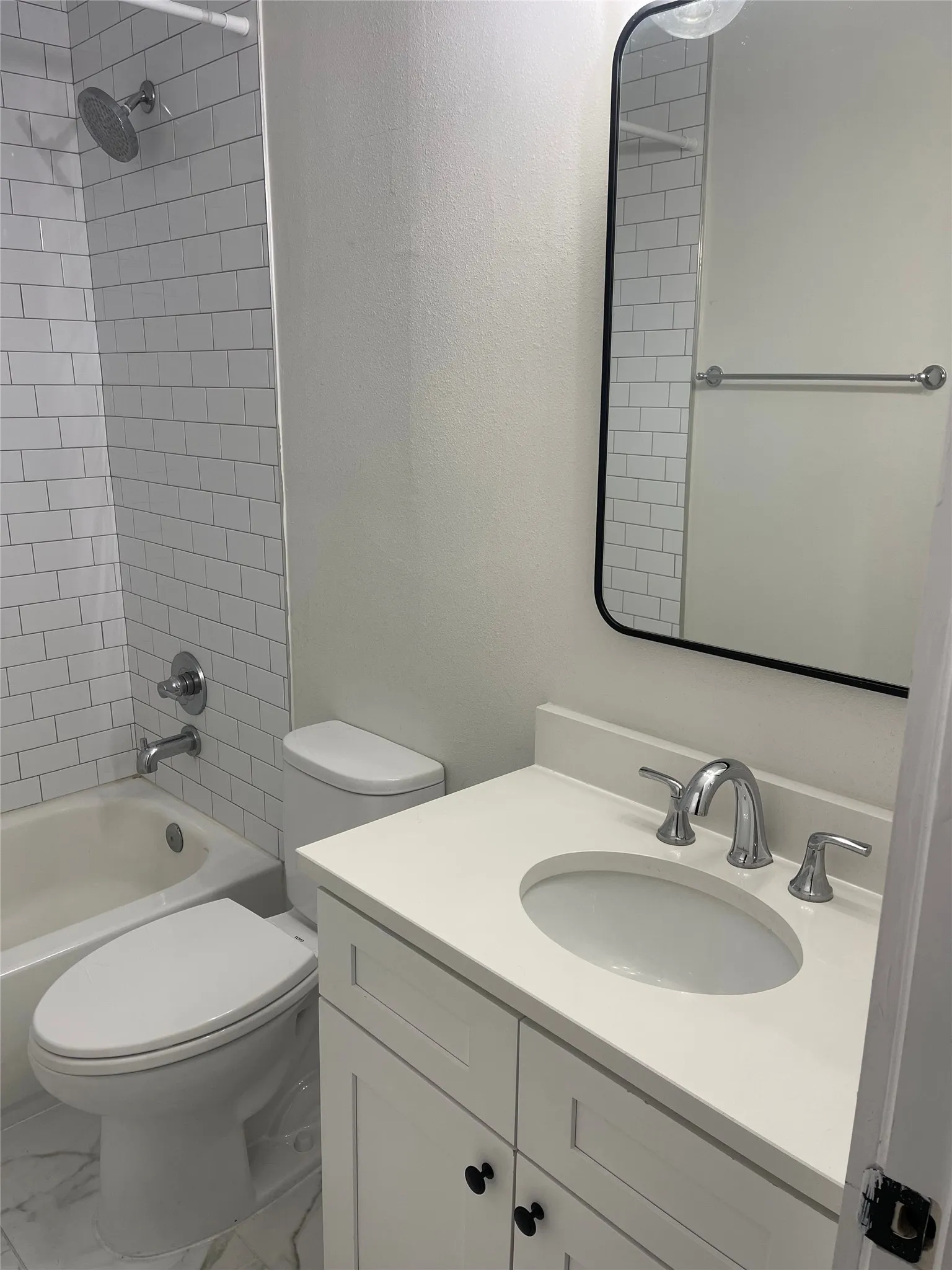Bathroom featuring a white subway tile shower surround, a built-in bathtub with chrome fixtures, a modern vanity with a white countertop and integrated sink, and a black-framed mirror