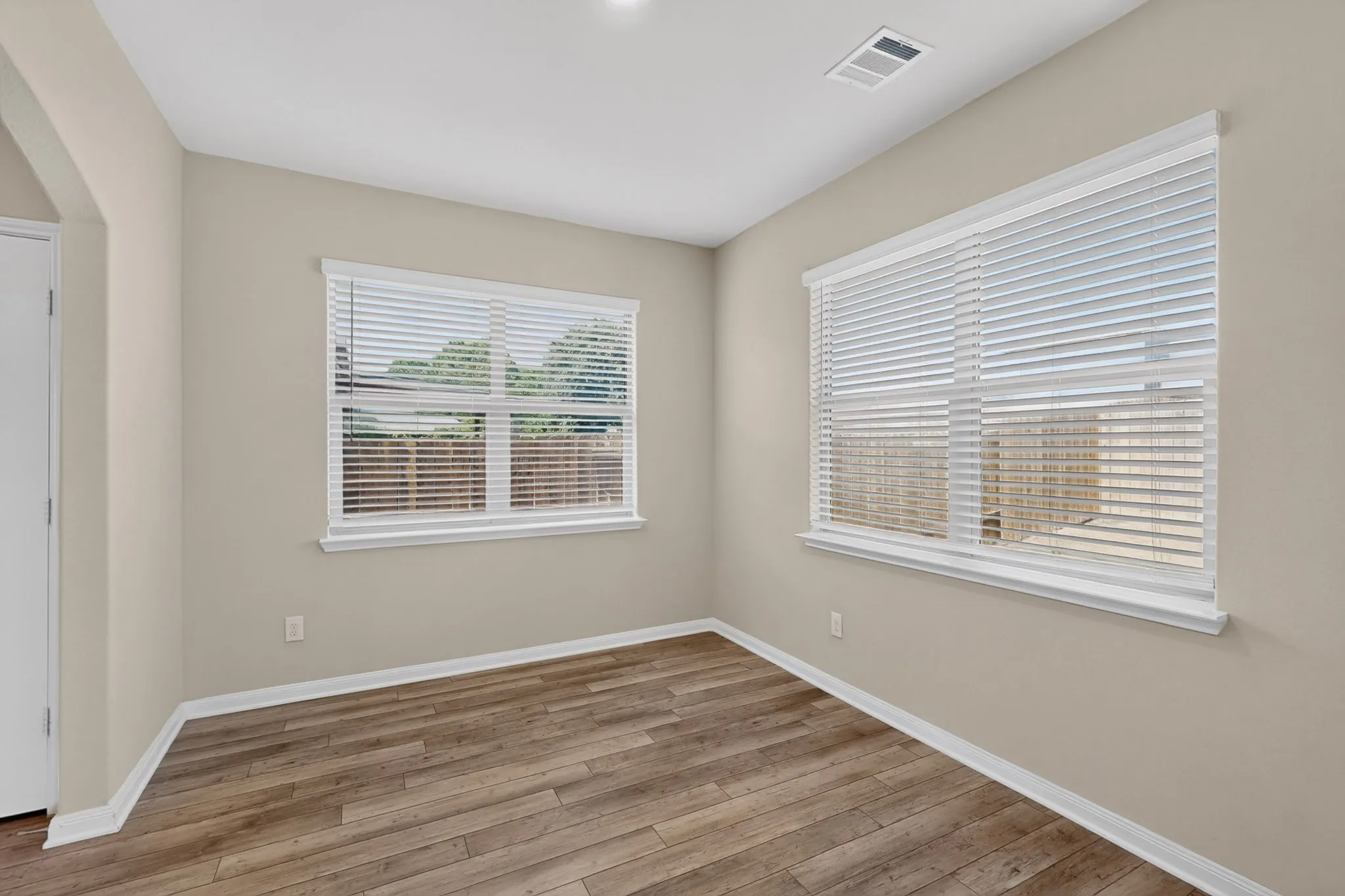 Room featuring wood-finish flooring, two windows with white blinds, neutral wall paint, white trim, and a ceiling light fixture