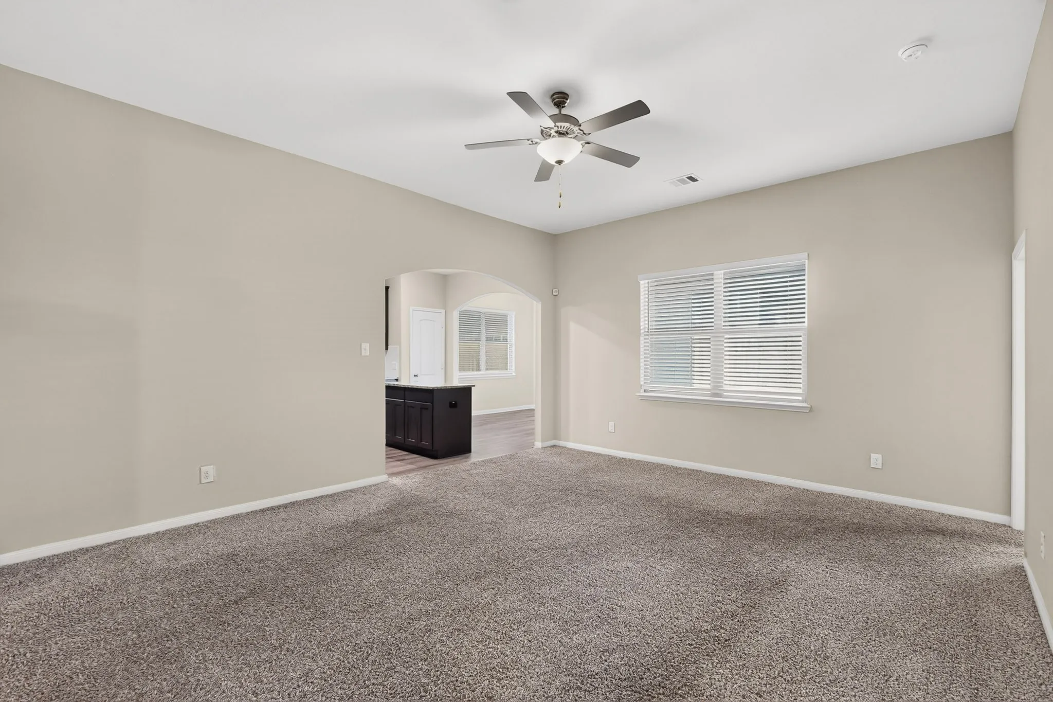 Spacious room featuring neutral carpeting, a ceiling fan with integrated lighting, and a window with horizontal blinds