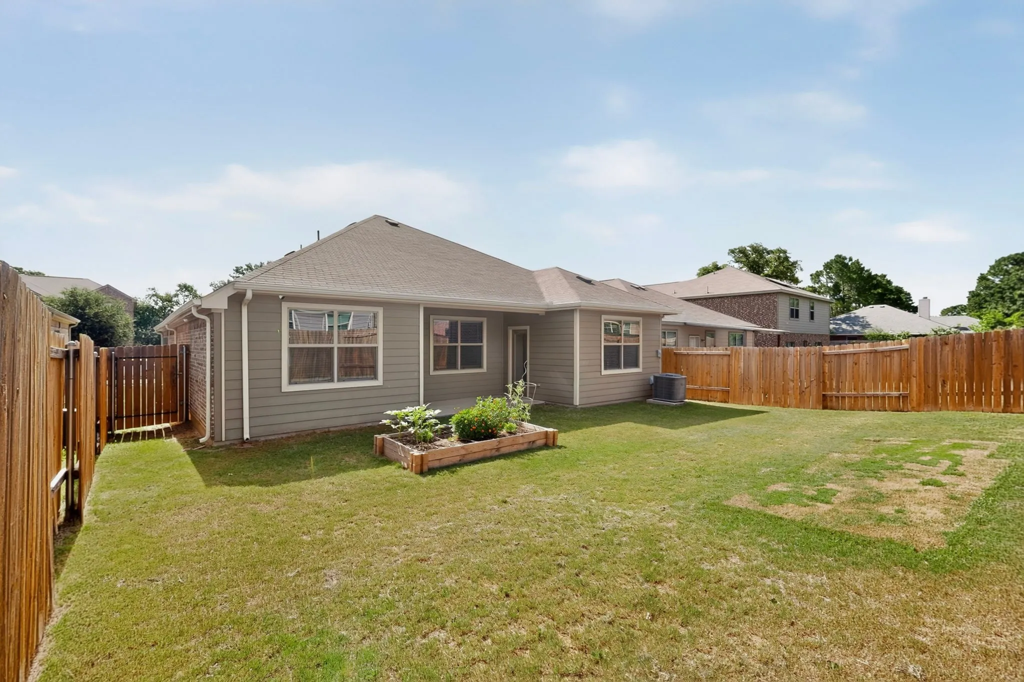 Expansive backyard featuring a manicured lawn, full wood fencing, and a built-in raised garden bed