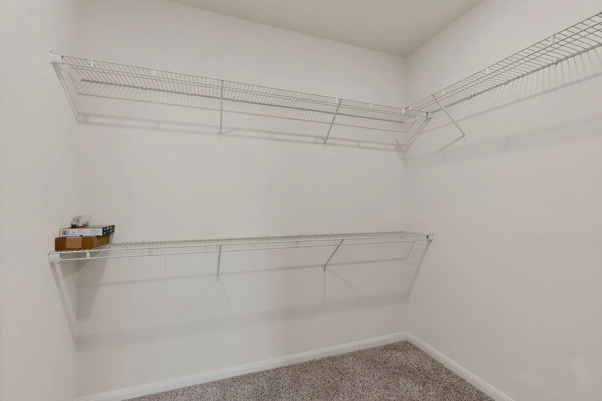 Spacious closet featuring two levels of white wire shelving, a corner shelving unit, and neutral-toned carpeting