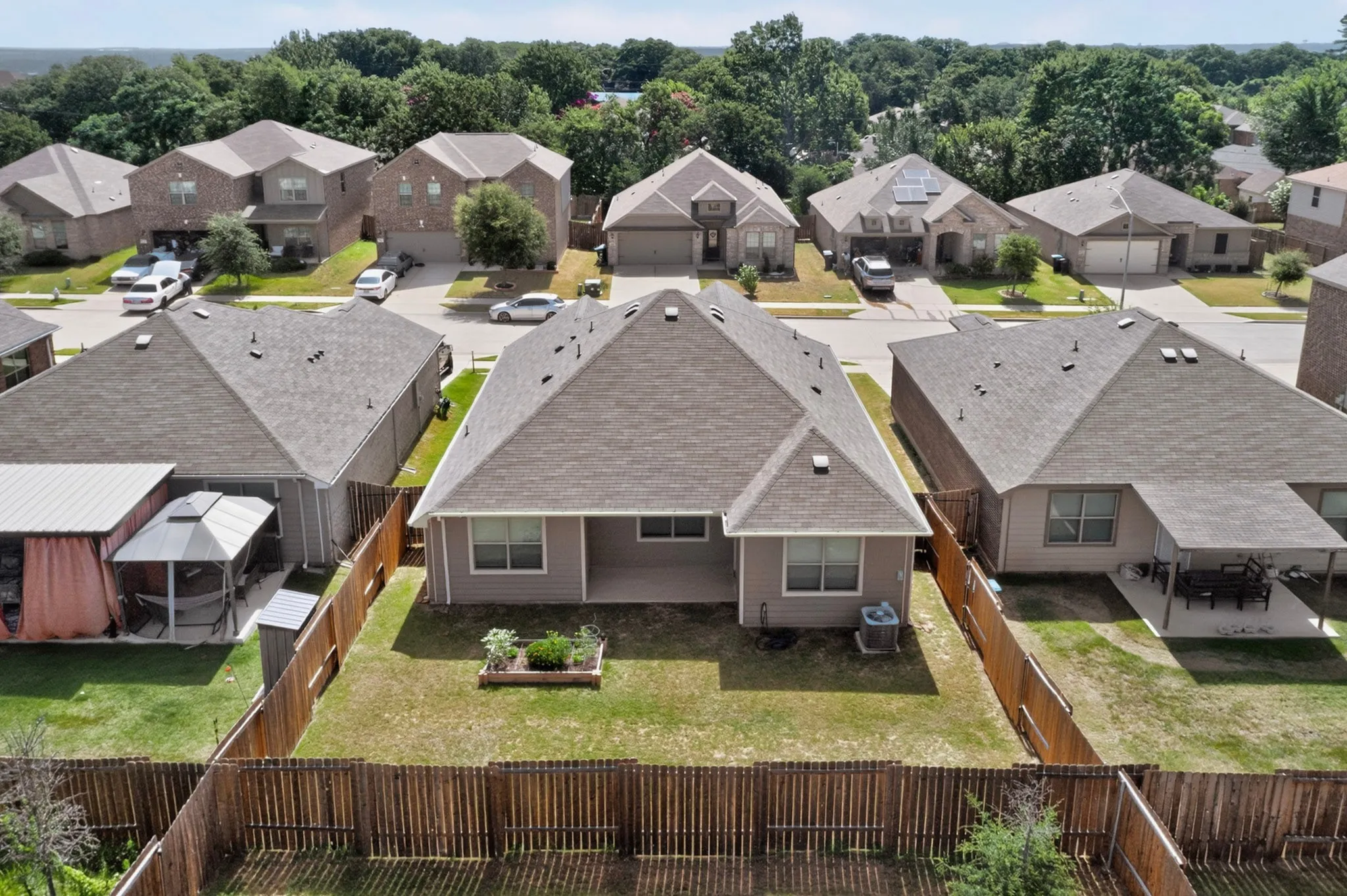 Fenced backyard with a covered patio, a raised garden bed, and a manicured lawn