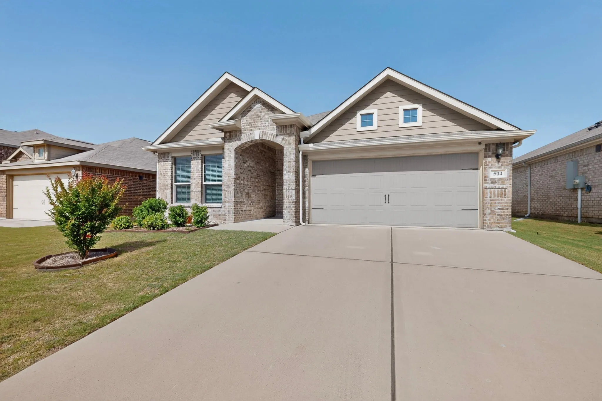 Brick and siding exterior featuring an arched entryway, gabled rooflines, and a two-car garage with a concrete driveway