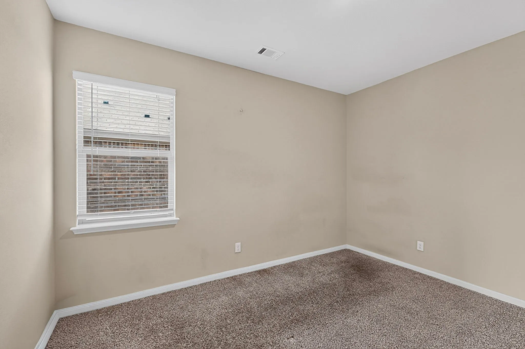 Neutral-toned interior with a single window featuring white blinds, complemented by light brown carpeting and white baseboards