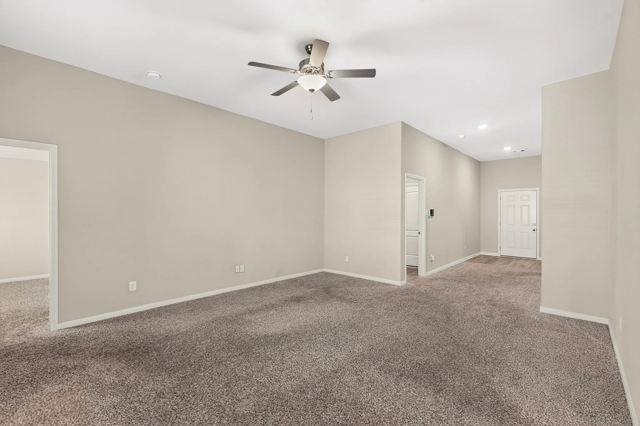 Spacious room featuring neutral carpeting, light-toned walls, and a ceiling fan with integrated lighting
