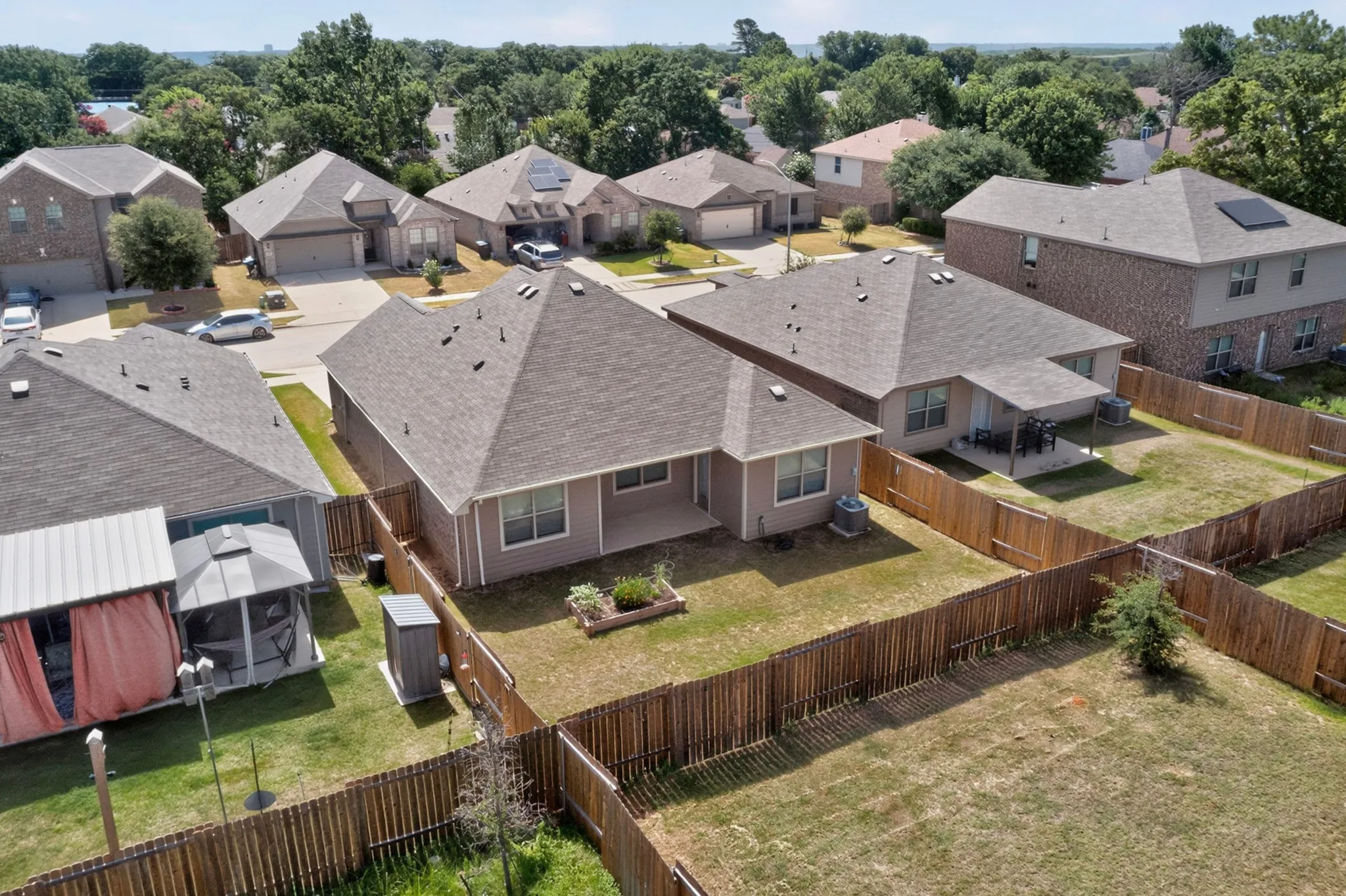 Fenced backyard featuring a covered patio, garden bed, and mature landscaping