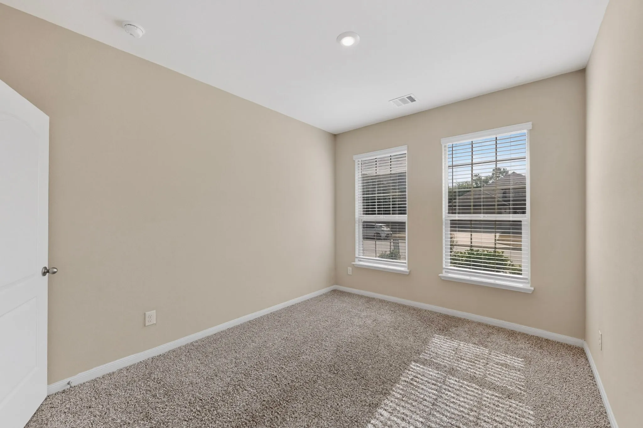 Neutral-toned room featuring two windows with horizontal blinds, recessed lighting, and light brown carpeting