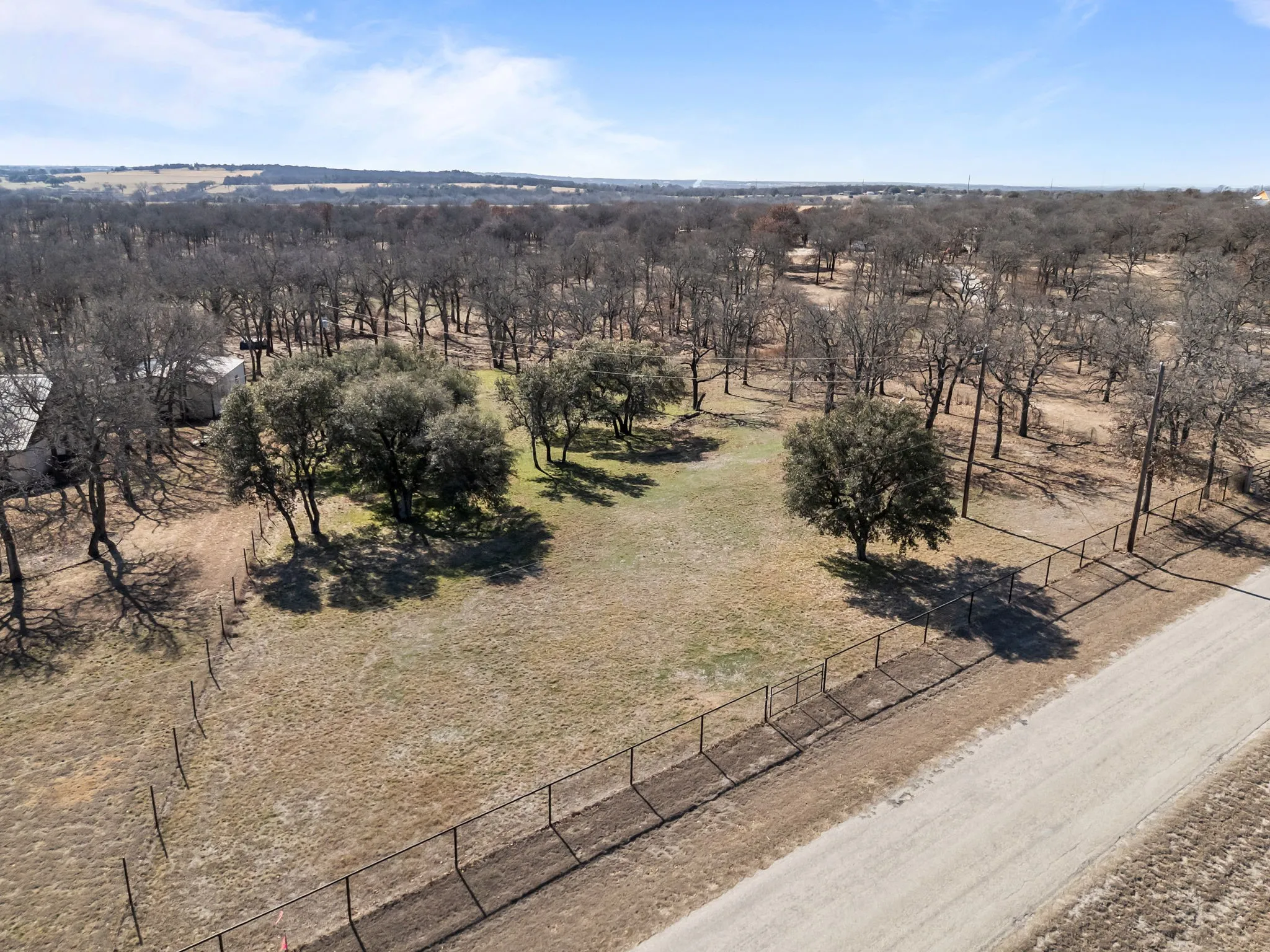 Expansive rural property featuring a perimeter fence, a gravel road frontage, and a mix of mature trees and open land